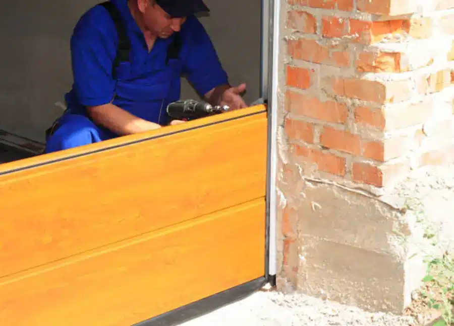 A man is replacing the garage door panel on a house with tools used to fix and install other doors.
